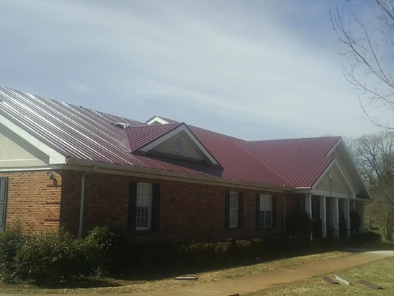 Red metal roof with gabled entries on a long brick building, from a Hail Damage Roof Repair job in Sound Beach