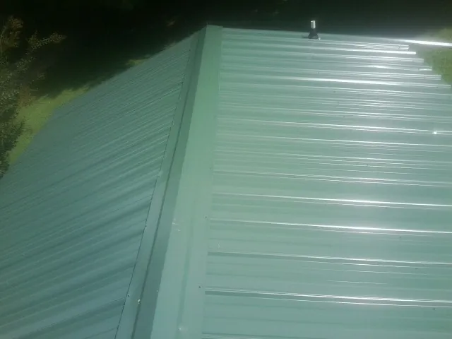 New green metal panels meeting at the ridge of a roof — Flat Roof Repair work by our crew in Sound Beach