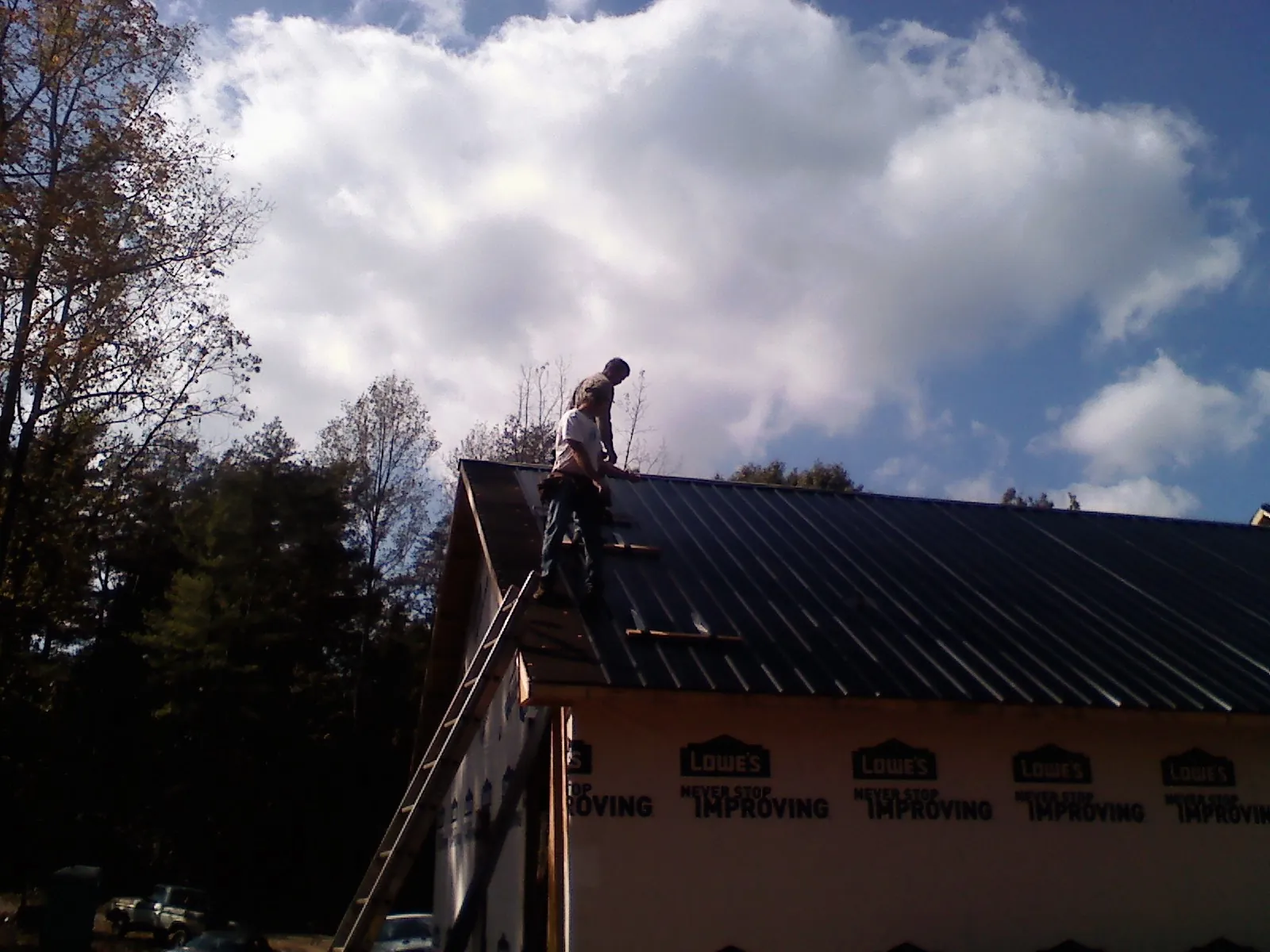Roofer fastening dark metal panels high against a cloudy sky, from a Roof Inspection job in Sound Beach