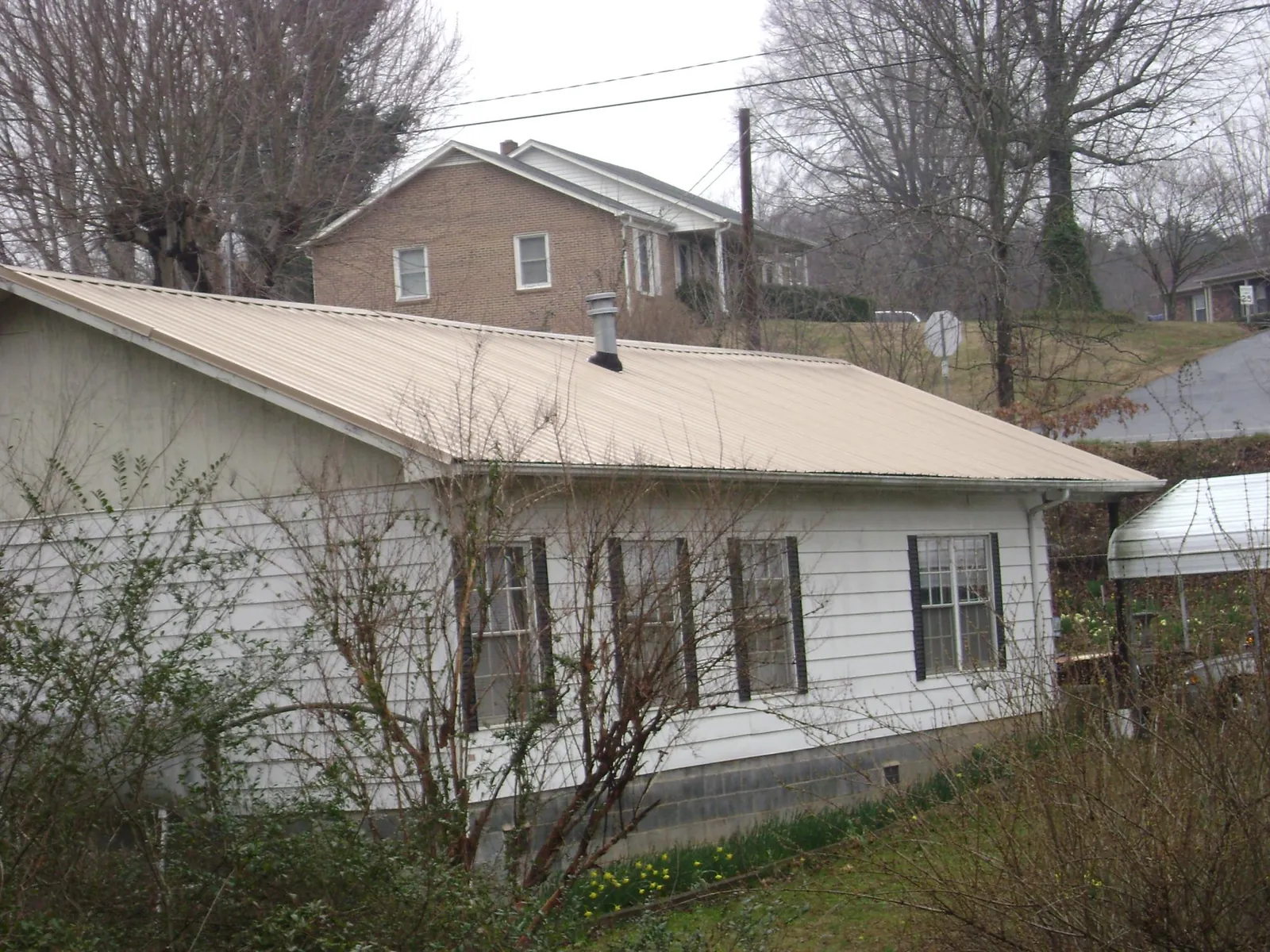 Tan metal roof on a white sided house set into a hillside — Commercial Roofing by Roofing Brothers in Sound Beach